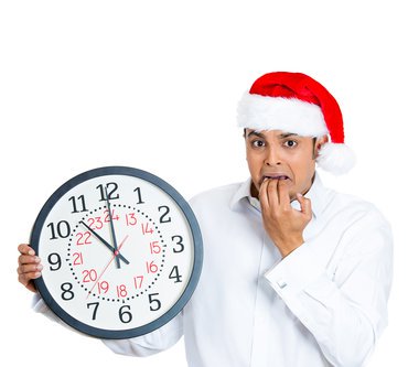 Man wearing a Santa hat and fretting over a clock he's holding, which shows that Christmas is almost here