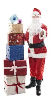 Санта-Клаус стоит рядом со стопкой подарков, указывая