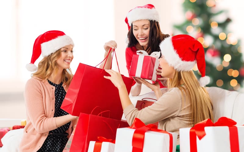 Group of women in Santa hats sitting among shopping bags and Christmas gifts